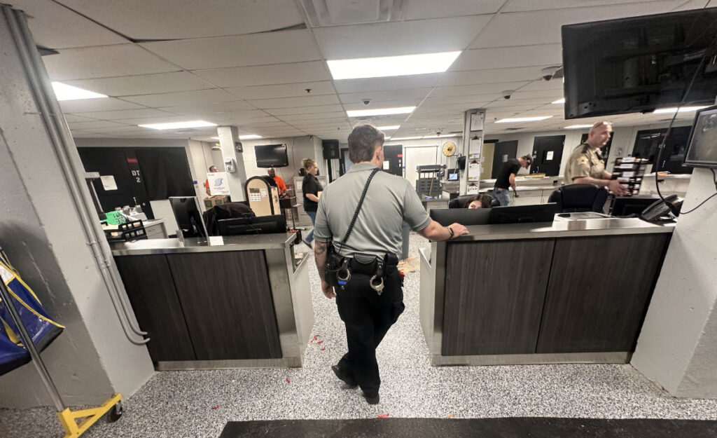 Security officer stands at a front desk in a busy lobby, with a tool belt and keys visible.