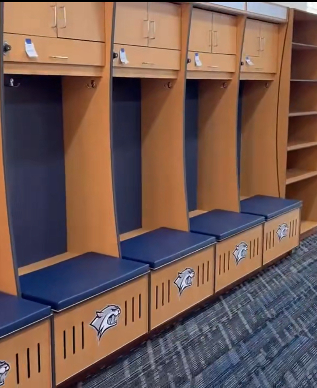 UNH_Soccer-06 - Legends Custom Lockers Row of wooden school lockers with blue cushioned benches and small top compartments, each featuring a Wildcats emblem on the bottom storage panel.